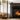 A cozy fireplace feature along a white living wall. The fireplace is burning and there's a stack of wood next to it.
